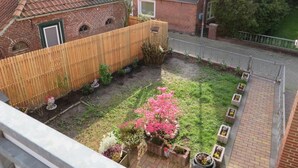 Un jardin à l’arrière de la maison, avec une clôture en bois, une maison en briques et un parterre de fleurs et d’arbustes.