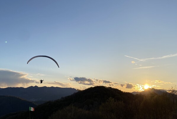 Un parapente survole un paysage montagneux, et on peut apercevoir un drapeau au sol.