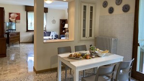 Un comedor con una mesa lista para el desayuno, una cocina con un radiador y una sala de estar con un sofá y un televisor.