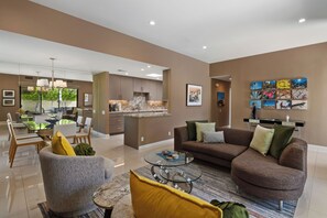 A modern living room with a brown sofa, a glass coffee table, and a dining area with a glass table and chairs.