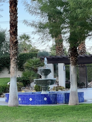 A fountain with water cascading into a basin, surrounded by palm trees and a blue tiled border. - Palm Springs, Greenhouse East! 2 Bdrs/2 Baths/ 25 Yard pool/Amazing location! (Palm Springs)