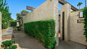 A narrow pathway leading to a building entrance with a textured wall and a sign indicating the address. - Palm Springs, Greenhouse East!  2 Bdrs/2 Baths/ 25 Yard pool/Amazing location! (Palm Springs)