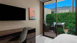 A hotel room with a desk, chair, and a large window with a view of a patio and mountains. - Palm Springs, Greenhouse East!  2 Bdrs/2 Baths/ 25 Yard pool/Amazing location! (Palm Springs)