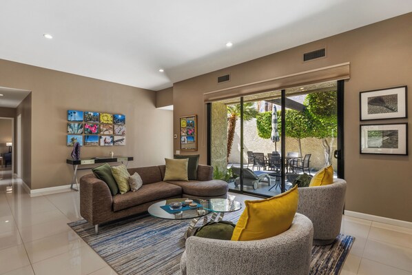 A modern living room with a sofa, armchairs, a coffee table, and a glass door leading to an outdoor patio.