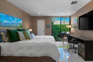 A bedroom with a bed, desk, and chair, a door, and a view of greenery outside. - Palm Springs, Greenhouse East! 2 Bdrs/2 Baths/ 25 Yard pool/Amazing location! (Palm Springs)