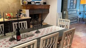 Un espace repas avec une longue table, des chaises blanches et une bouteille de vin.