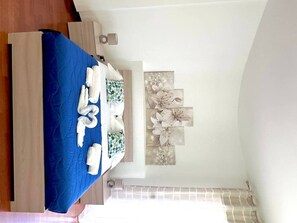 A bedroom with a blue bedspread, neatly arranged towels, and a wall-mounted artwork of flowers.
