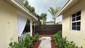 A narrow pathway flanked by green shrubs leading to a house with a white exterior and a wooden fence in the background. - CHARMING INDEPENDENT GUEST HOUSE (West Palm Beach)