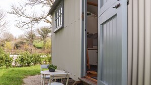 Een laag, klein gebouw met een houten terras en een tafel met stoel erbij.