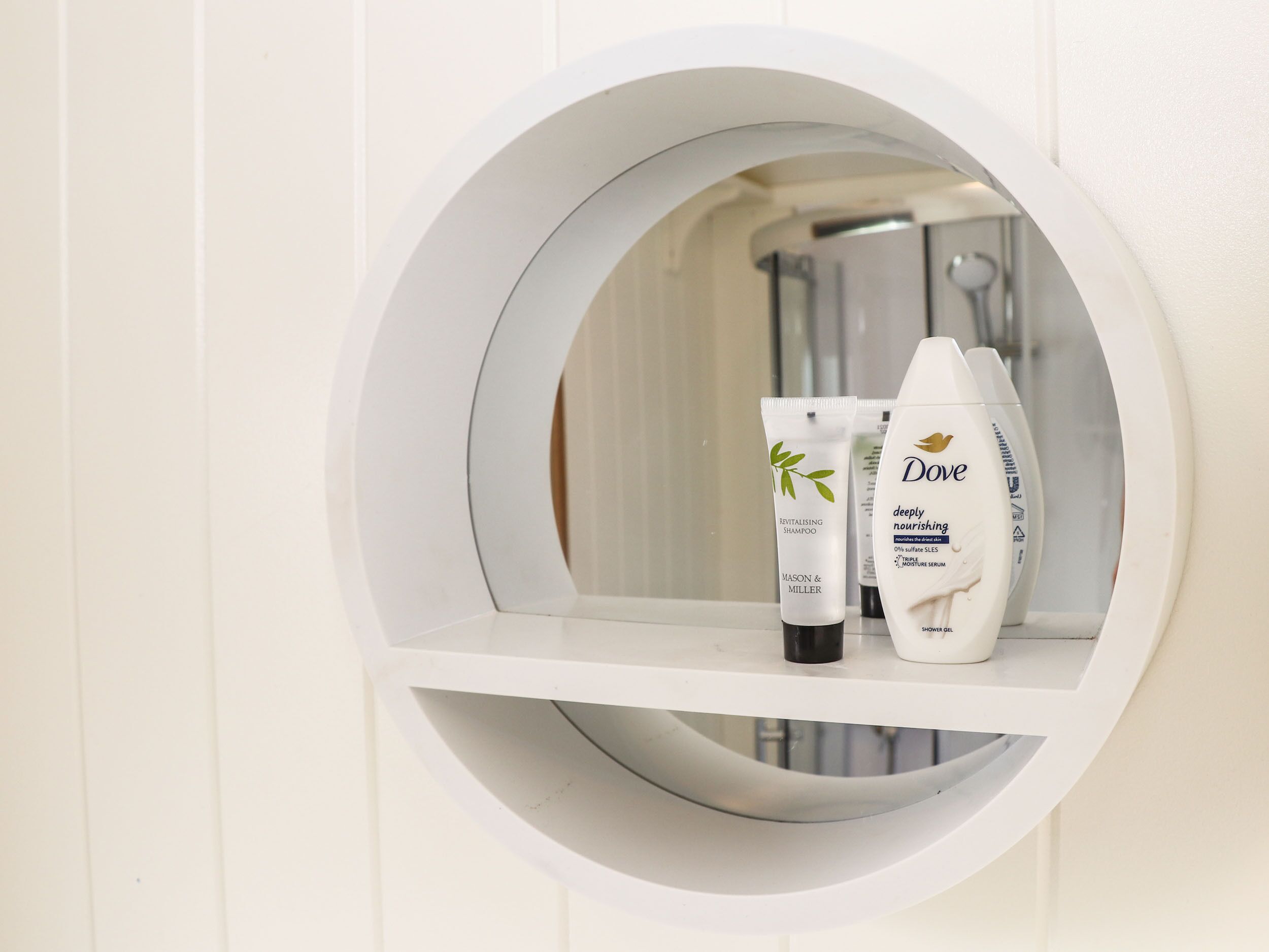 Ein Badezimmer mit einem runden Ablagefach für Kosmetikartikel, auf dem eine Dove-Shampoo-Flasche und eine Lotiontube stehen.