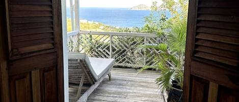 A wooden deck with a white bench and potted plants, leading to a view of the ocean.