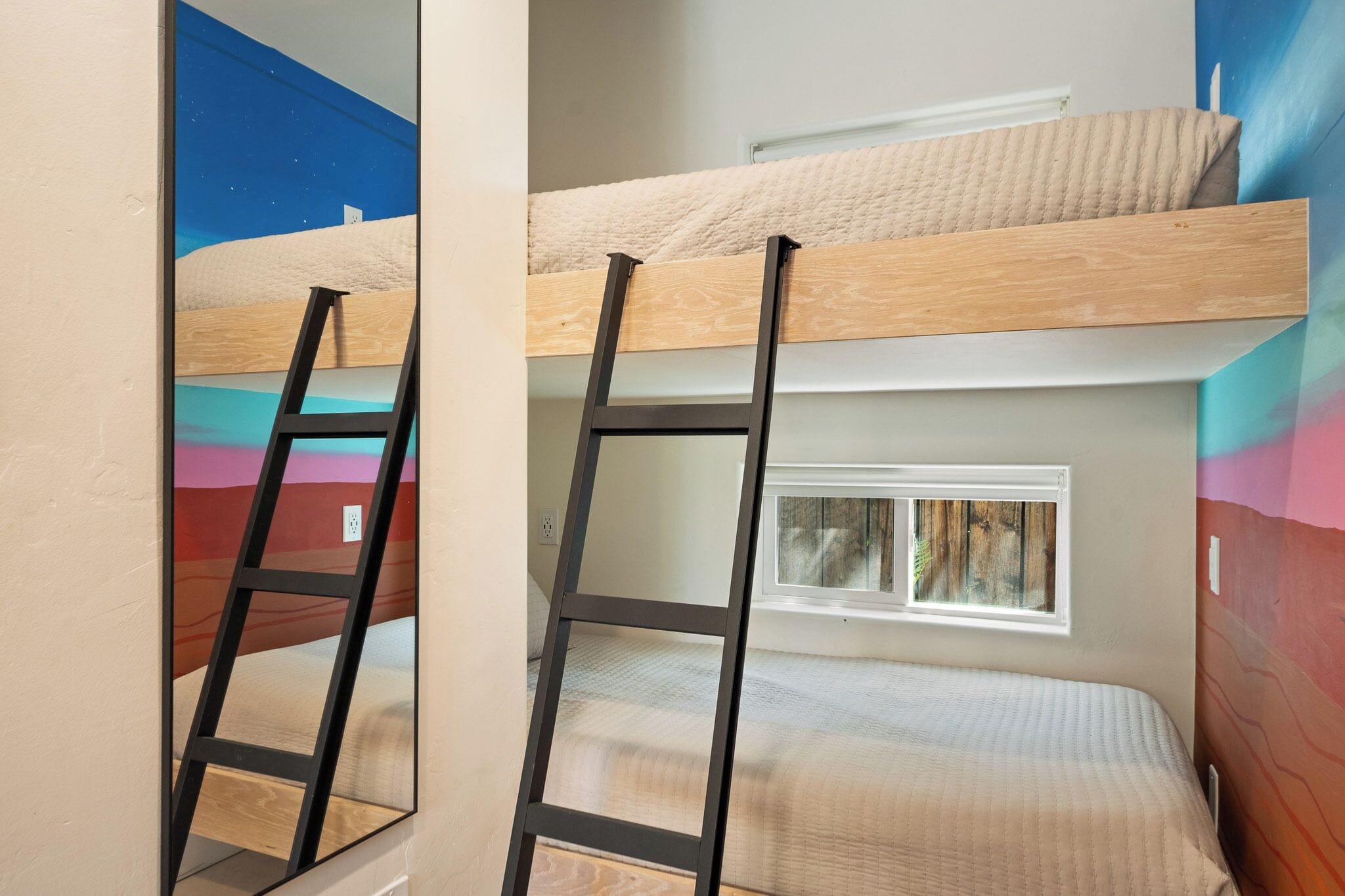 Ein Stockbett mit Fenster, einer Leiter und einer Wand mit einem farbenfrohen Wandbild.