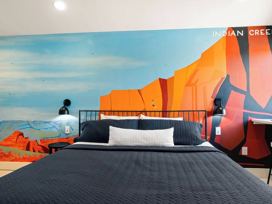 A bedroom with a bed, a desk, and a mural on the wall.