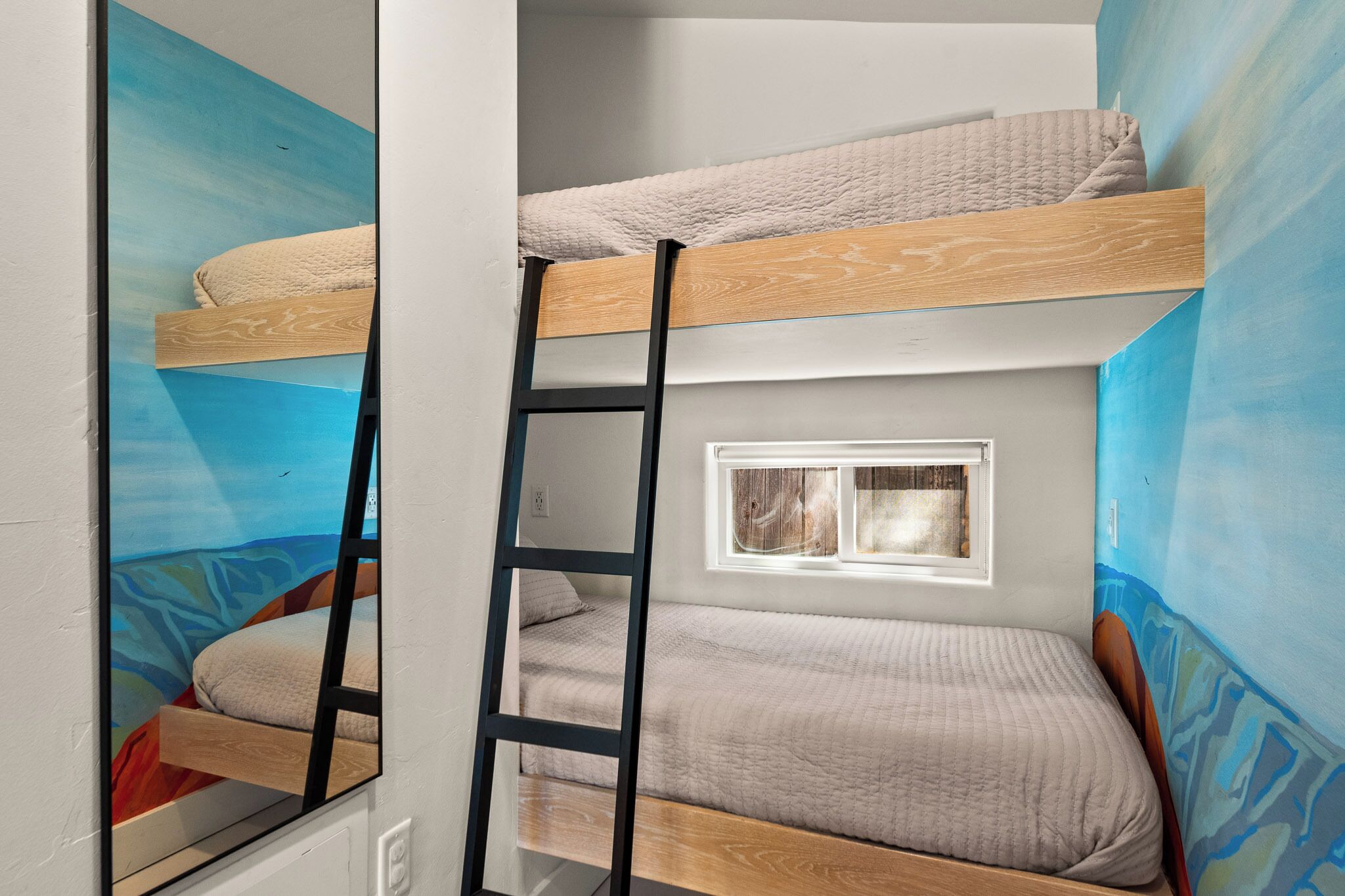 A bunk bed with a ladder, a window, and a mural on the wall.