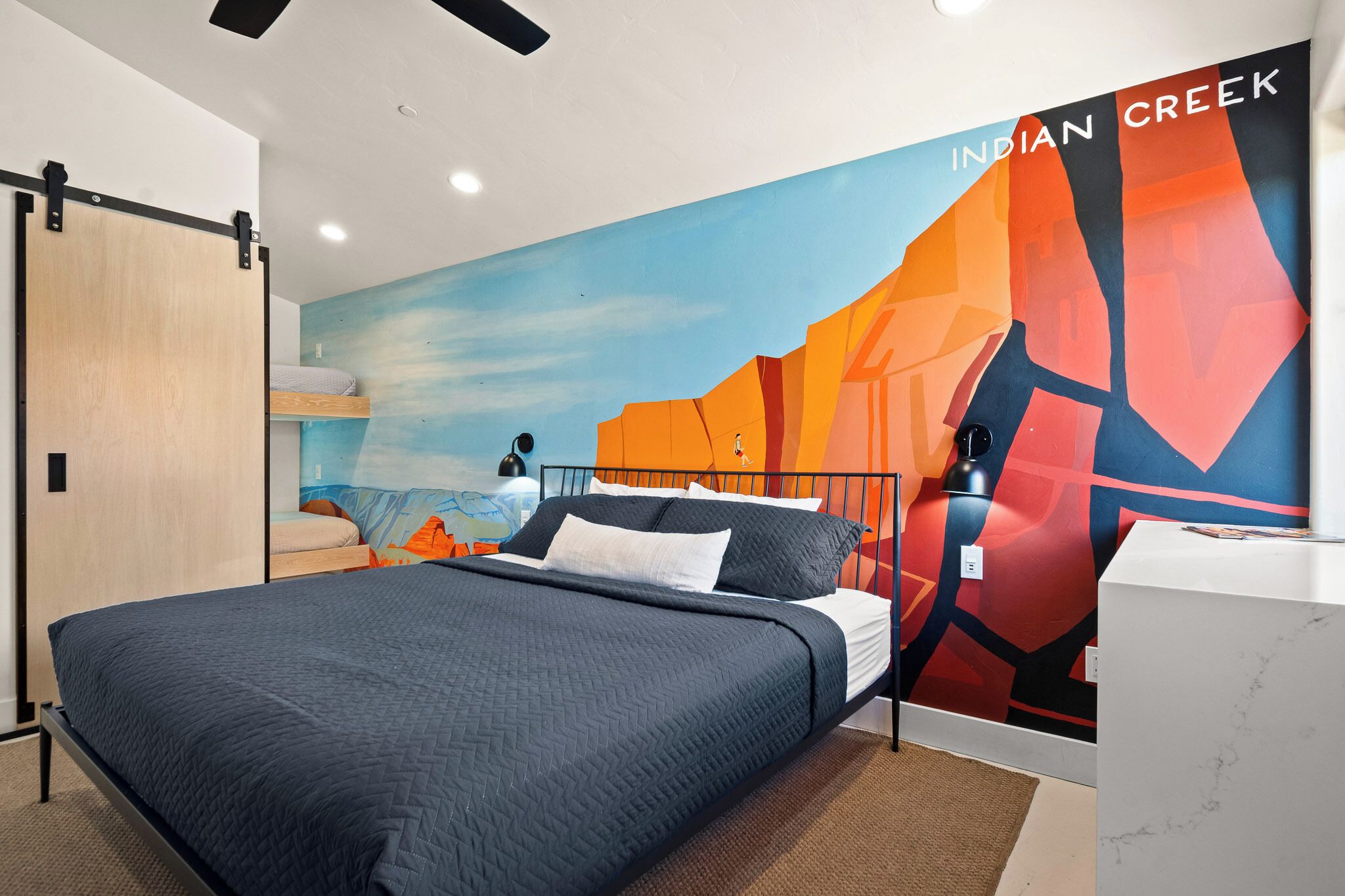 Une chambre d’hôtel moderne dotée d’un grand lit, d’un bureau et d’une fresque représentant un paysage désertique.