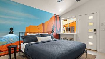 A modern bedroom with a large bed, a desk, and a mural on the wall.