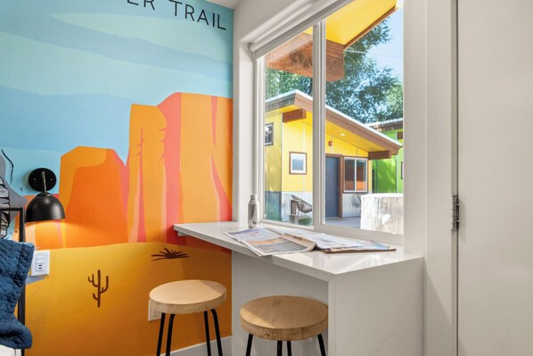 A room with a colorful mural, a window with a view of a yellow building, and two stools.