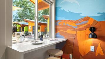 A kitchen with a window, a mural, and a countertop with a plate and a can.