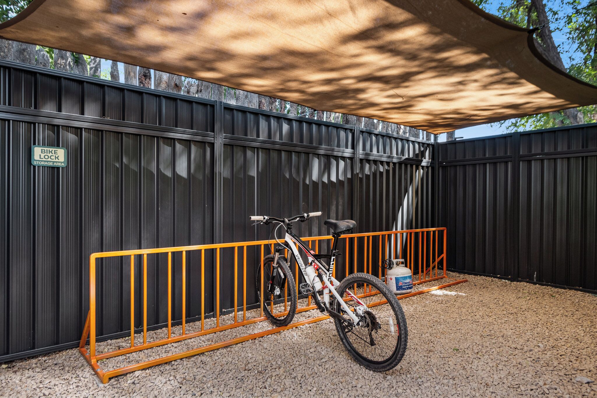 A bike lock and a gas canister near a bike rack under a shaded area.