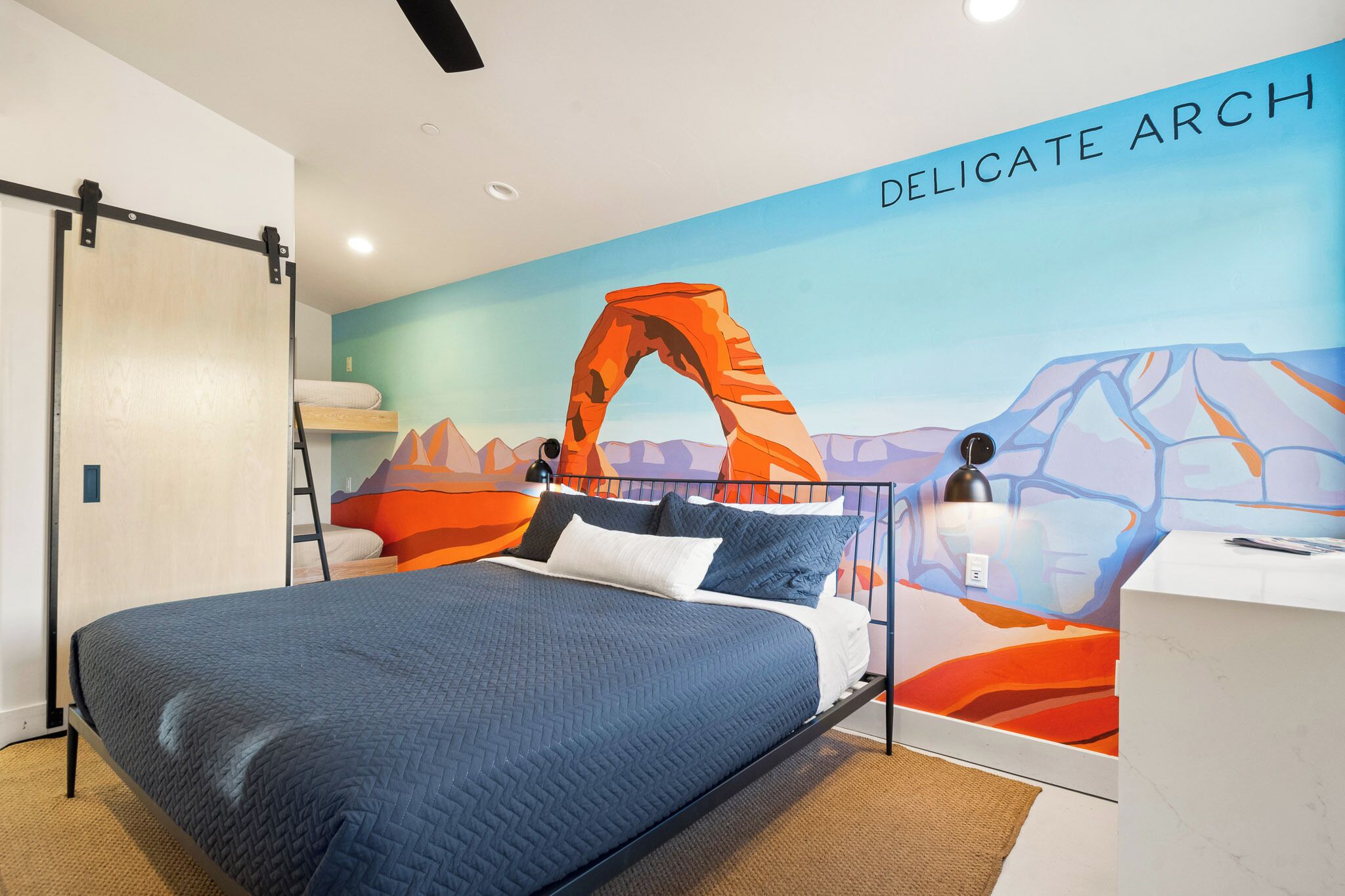 A modern bedroom with a bed, a desk, and a mural of a mountain landscape.