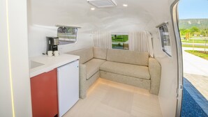 A compact kitchen with a refrigerator, a coffee maker, and a window with curtains.