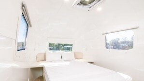 A modern, minimalist bedroom with a single bed, a window with a view of houses, and a small table.