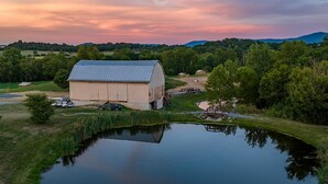 A large barn with a flat roof, surrounded by a pond and greenery.