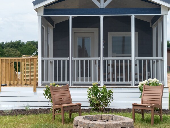 A covered porch with two wooden chairs and a stone fire pit.
