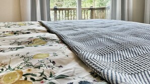 Un lit avec une literie à motifs floraux et une couverture à motifs géométriques, une fenêtre avec des rideaux et une vue sur la verdure à l’extérieur.