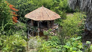 A small, rustic gazebo with a tiled roof surrounded by lush greenery and a variety of plants. - HOTEL KALMA  (Santa Fe de Antioquia)