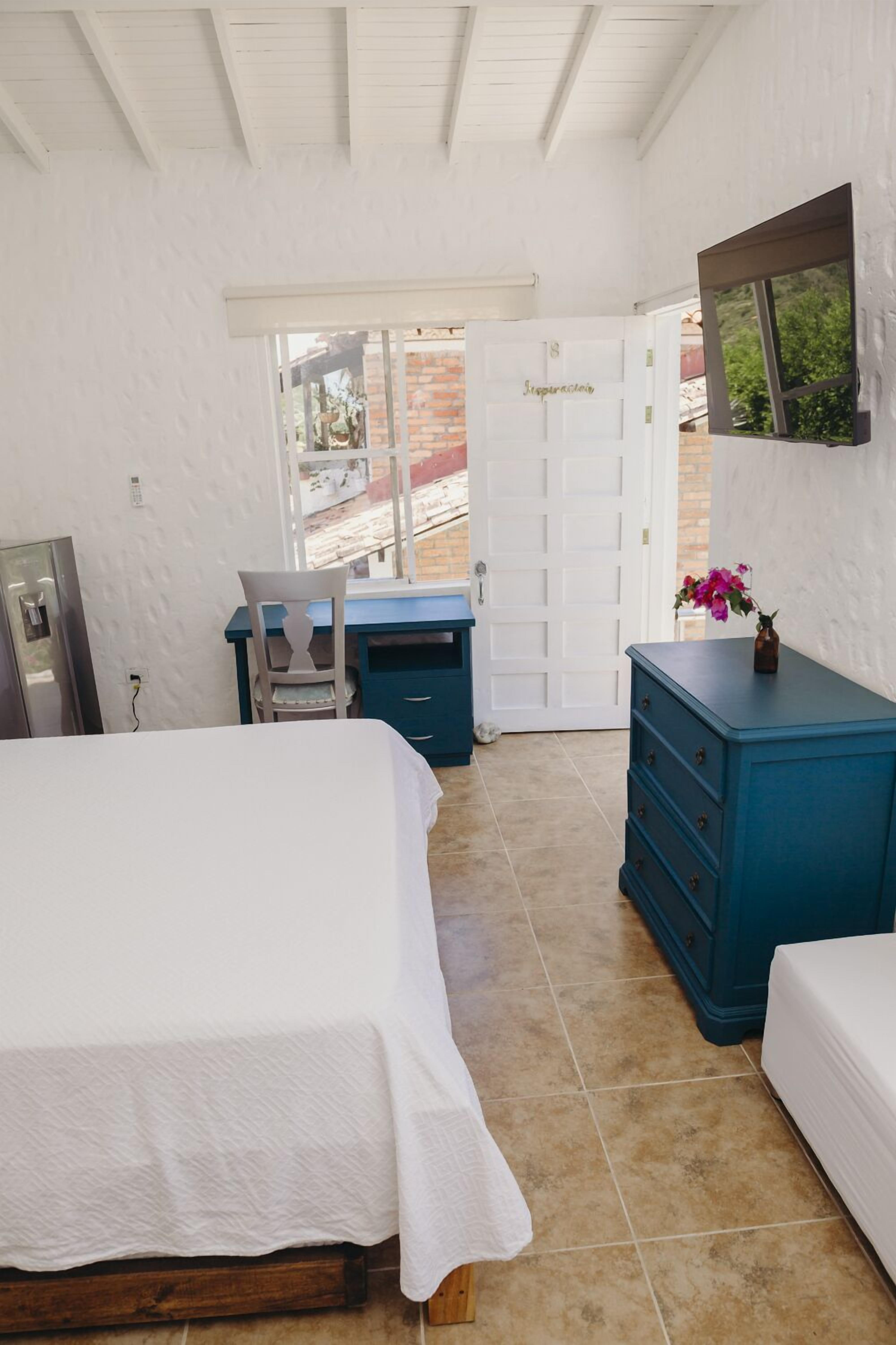 A bedroom with a bed, a desk, a dresser, and a door leading to an outdoor area.