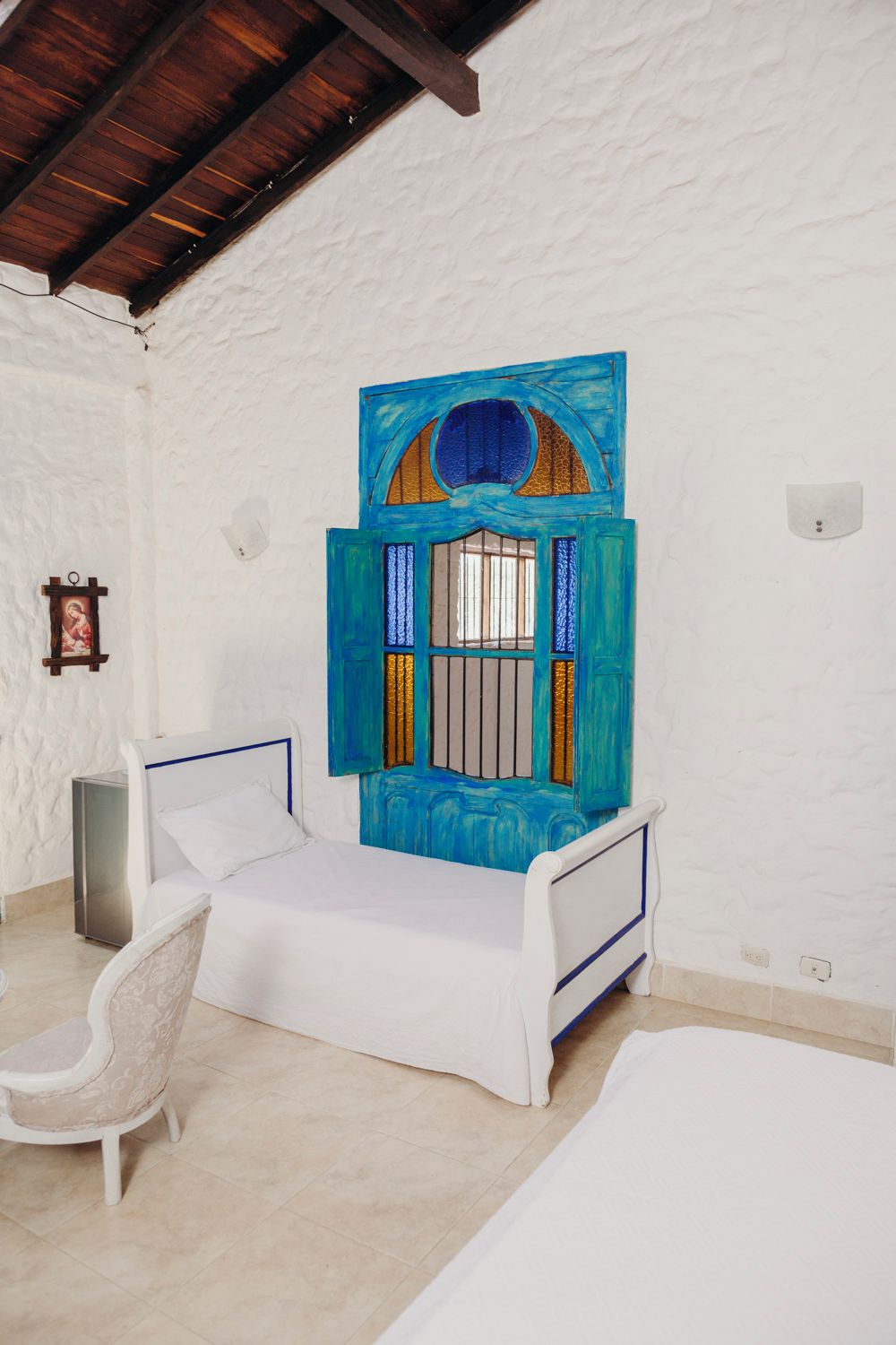 A room with a bed, a chair, and a wall-mounted artwork.