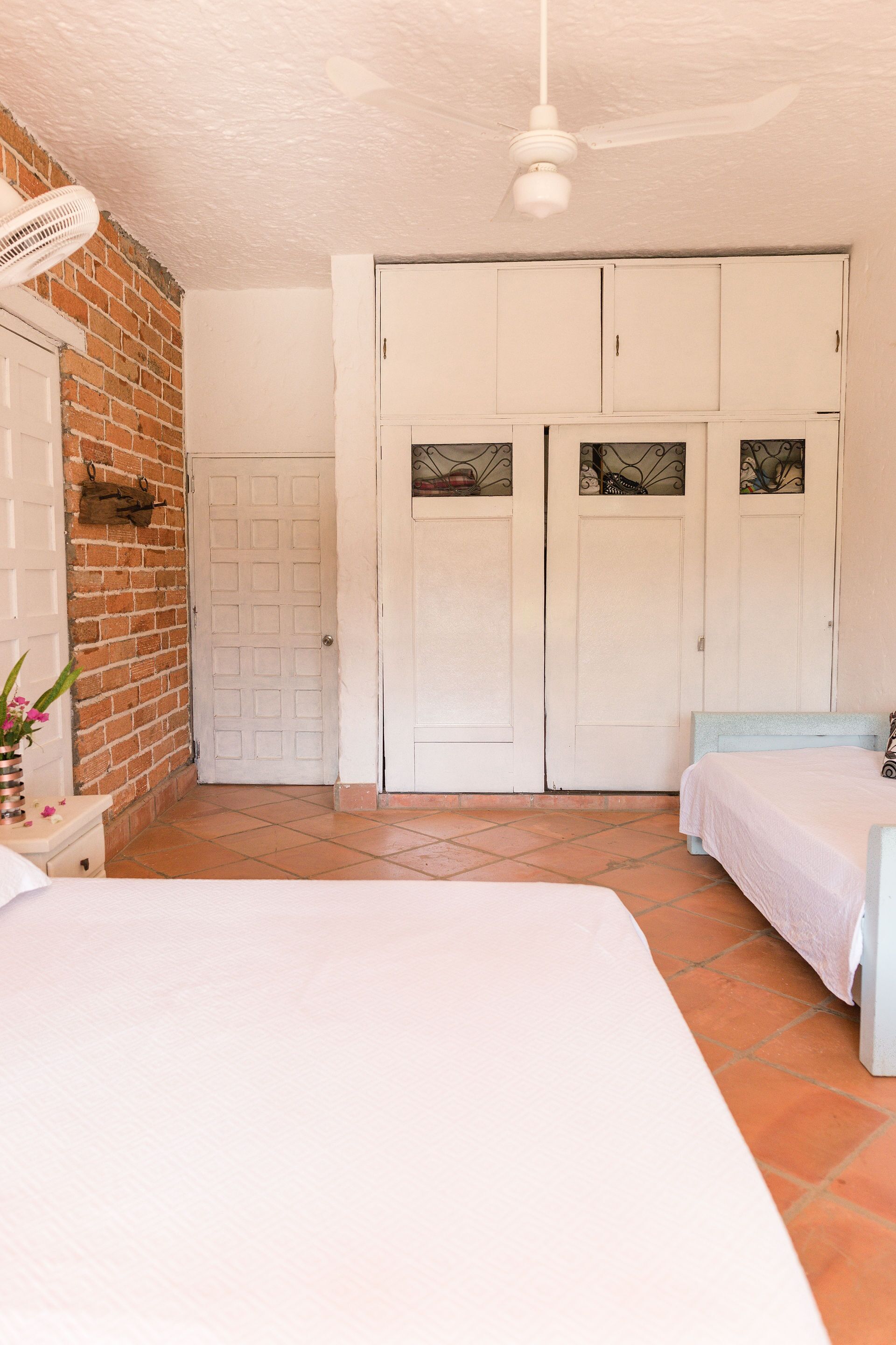 A bedroom with a brick wall, white wardrobe, and a ceiling fan.