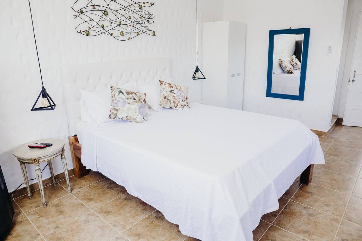A bedroom with a large bed, a small table, a wardrobe, and a mirror on the wall.