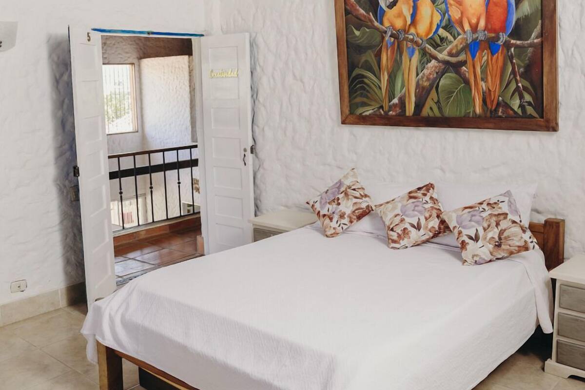A bedroom with a bed, a door, and two paintings.