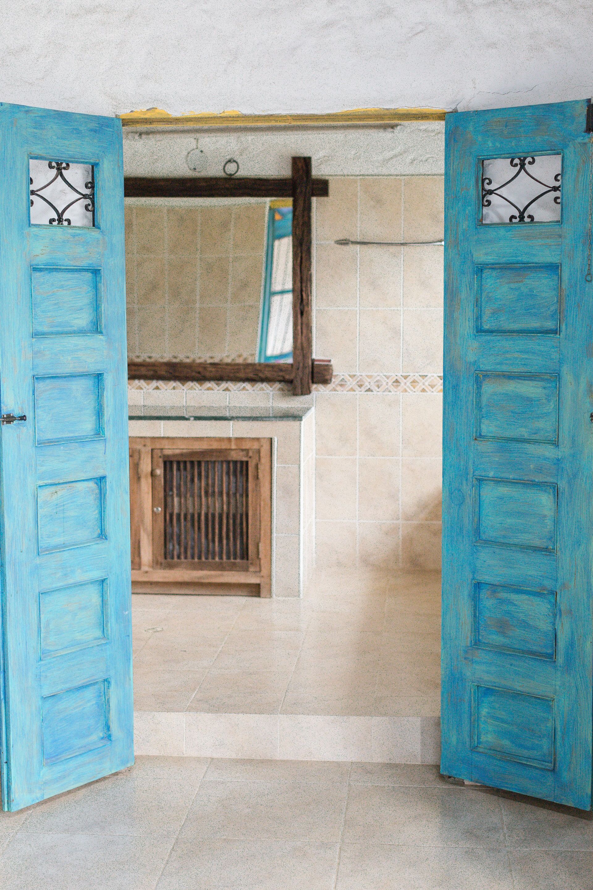 A room with a tiled floor, a wooden door with a metal handle, and a window with a decorative metal grille.