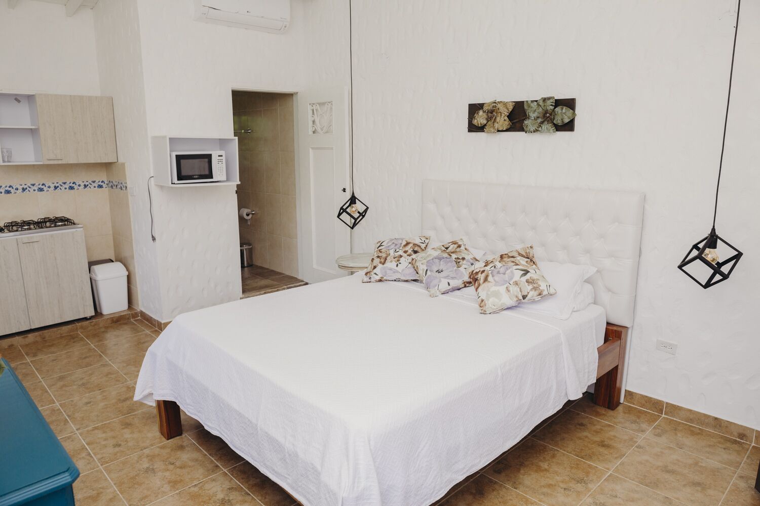 Een slaapkamer met een bed, kussens, een magnetron, een toilet en een wastafel.