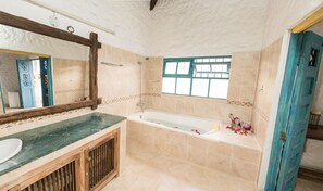 Un baño con bañera, tocador de madera, espejo grande y ventana con detalles azules.