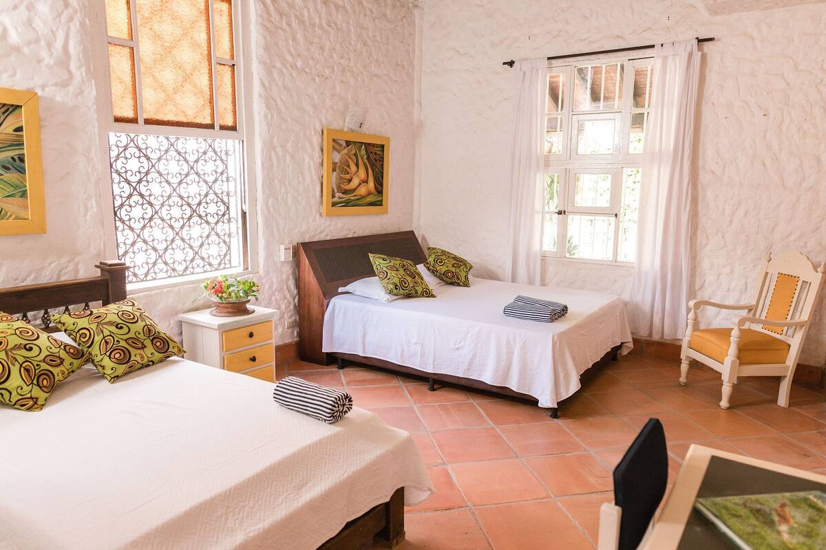 A bedroom with two beds, a chair, a nightstand, and a window with curtains.