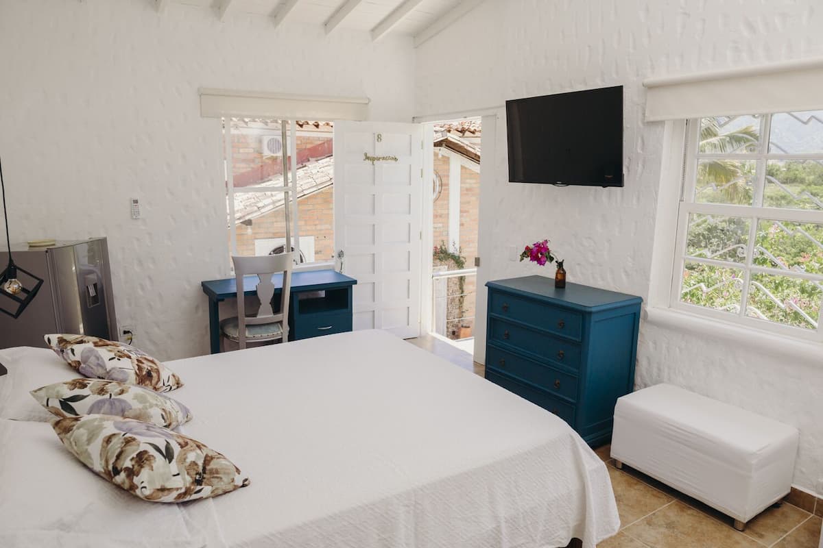 A bedroom with a bed, a desk, a dresser, a TV, and a window with a view.