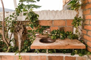 Un área de estar al aire libre de estilo rústico con una mesa de piedra y un cuenco, rodeada de exuberante vegetaci ón y un muro de ladrillo.