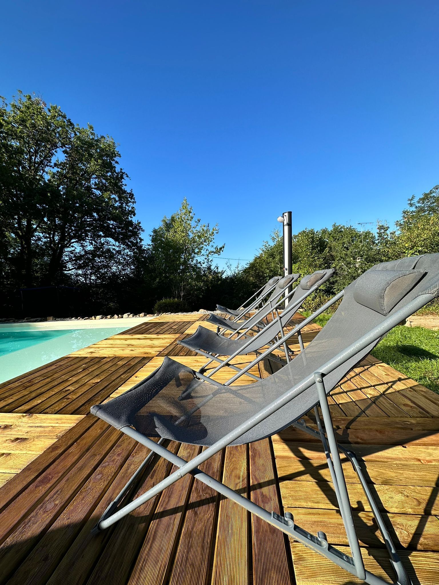 A wooden deck with lounge chairs facing a pool.
