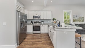 A modern kitchen with white cabinets, stainless steel appliances, and a wooden floor. - Modern Condo in Heart of Downtown Fuquay (Fuquay-Varina)