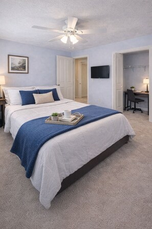 A bedroom with a bed, a desk, a chair, a television, and a ceiling fan.