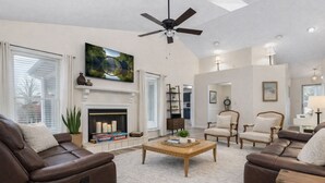 Ein Wohnzimmer mit Kamin, Ledersofas, einem Couchtisch und Deckenventilator.