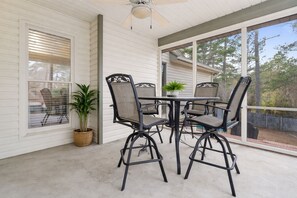 A covered patio with a table and chairs, a ceiling fan, and a view of trees.