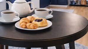 Eine Küche mit dunkelblauen Schränken, einem weißen Teekessel, zwei Kaffeetassen und einem Teller Croissants.