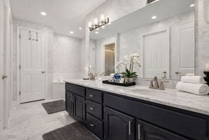 A modern bathroom with a large mirror, two sinks, dark cabinets, and a marble floor.