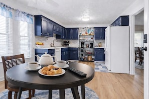 Une cuisine moderne avec des meubles bleus, un réfrigérateur blanc et une table à manger où sont disposés des croissants et du café.