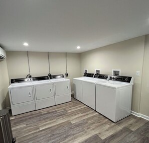 A laundry room with four stacked washer and dryer units, a trash can, and a ceiling-mounted air conditioning unit.